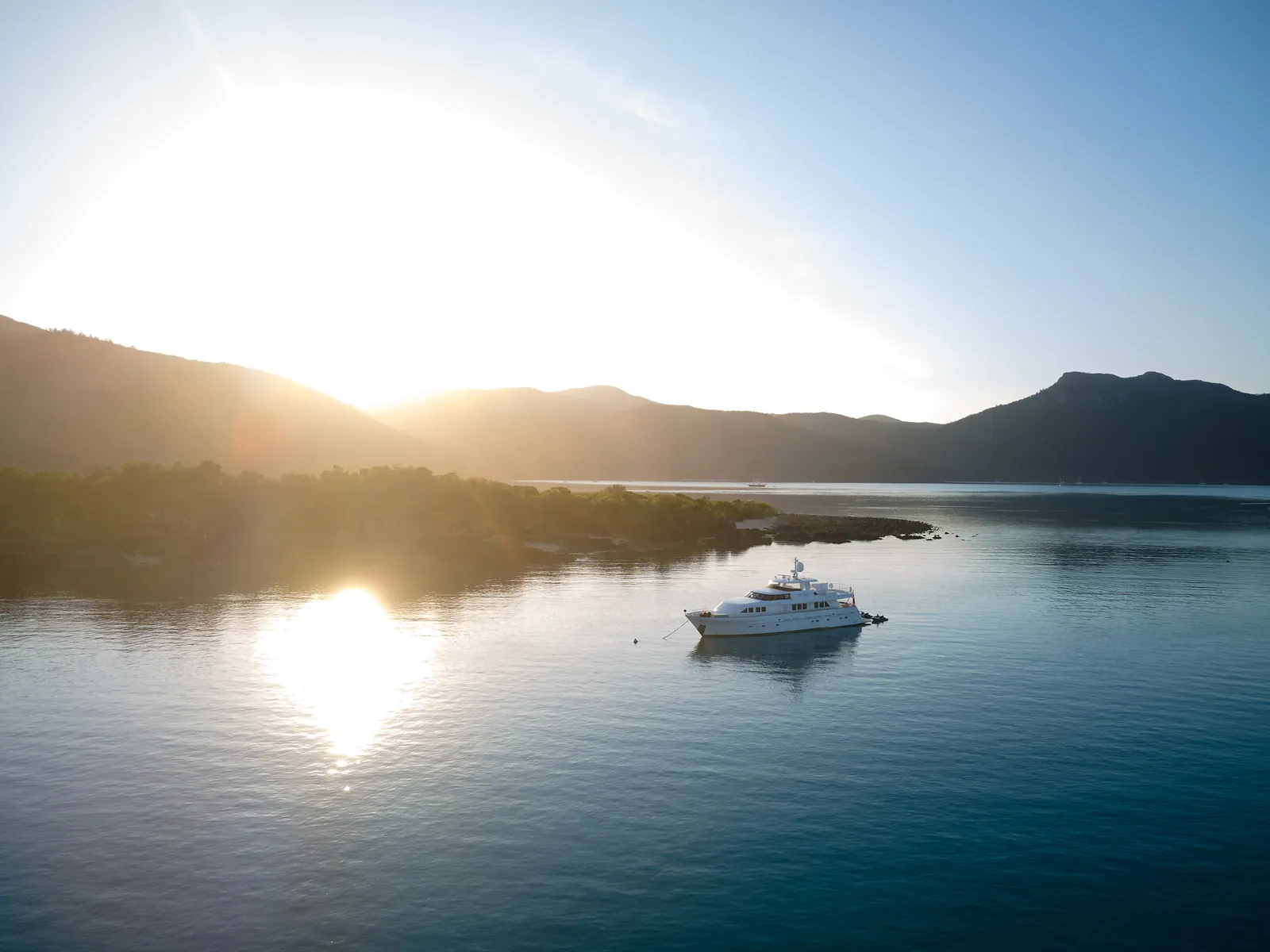 M/Y Sea Raes, at anchor from the air, the sun low over the hills